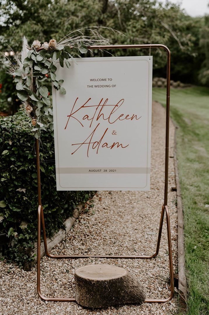 Wedding under 40k with white wedding welcome sign on a copper frame and foliage decor 