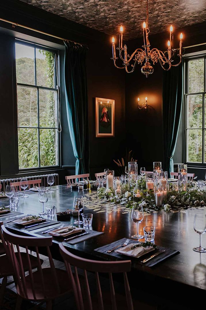 Reception room of Netherbyres House Scottish wedding venue with dark tones, gold framed alternative wedding photos and windows overlooking manicured lawns 