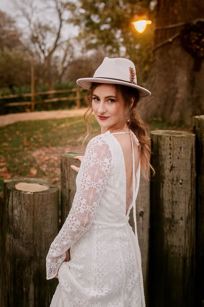 Boho bride wearing a long sleeve lace wedding dress with cream hat with feathers 