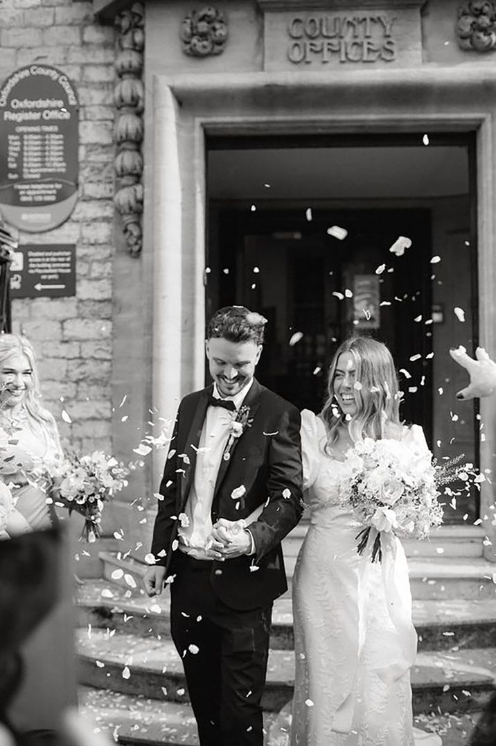 Groom in black tie and bride in Story of My Dress wedding dress exit their registry office wedding to confetti