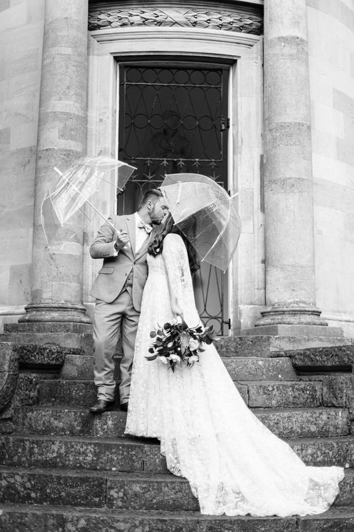 Bride and groom under clear umbrellas on their rainy wedding day 