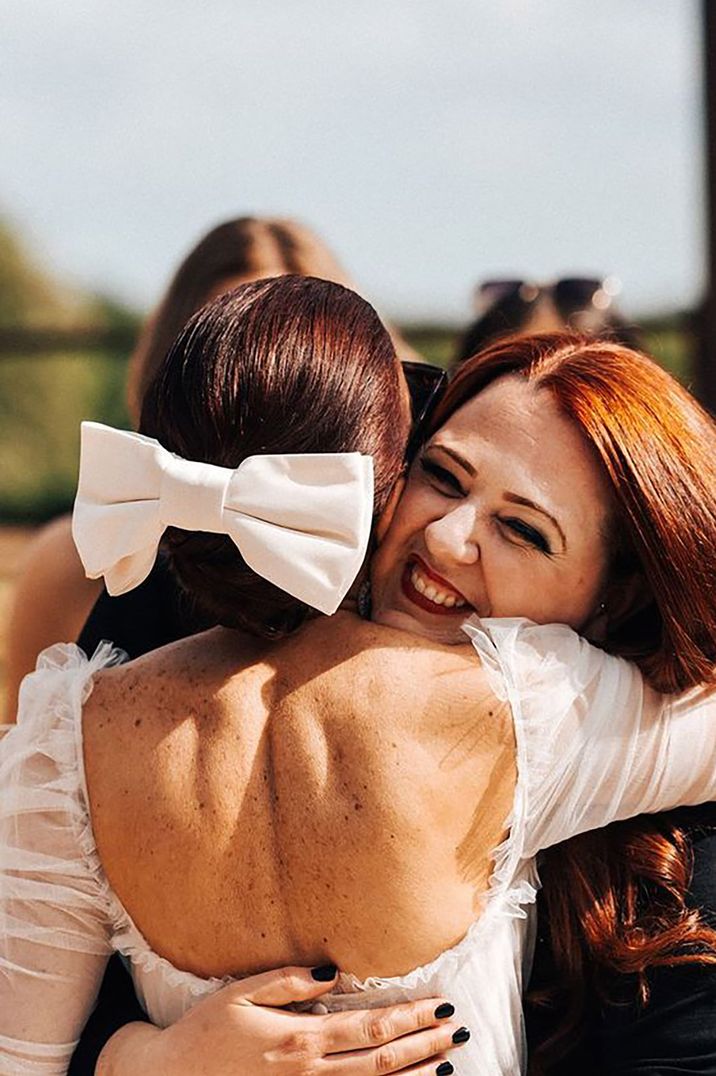 Image of bride hugging a guest while wearing a white bow hair accessory by Christophe Bourgeois Photography