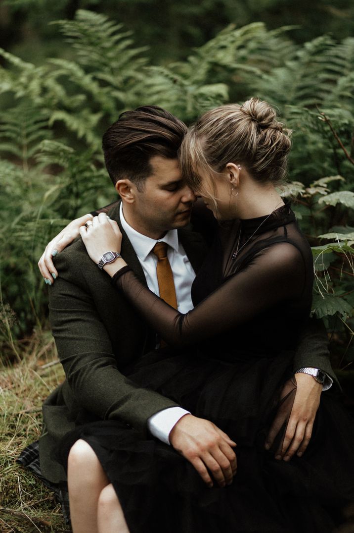 Bride and groom embrace intimately with the groom in a green suit jacket and kilt with the bride in a black wedding dress