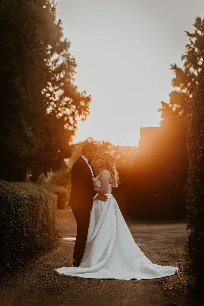 Bride in strapless wedding dress with groom in black tuxedo posing for couple portrait at golden hour 