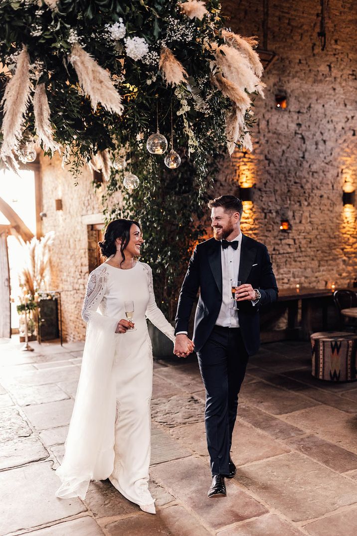 The bride and groom walk into the rustic barn wedding venue decorated with hanging floral installation 