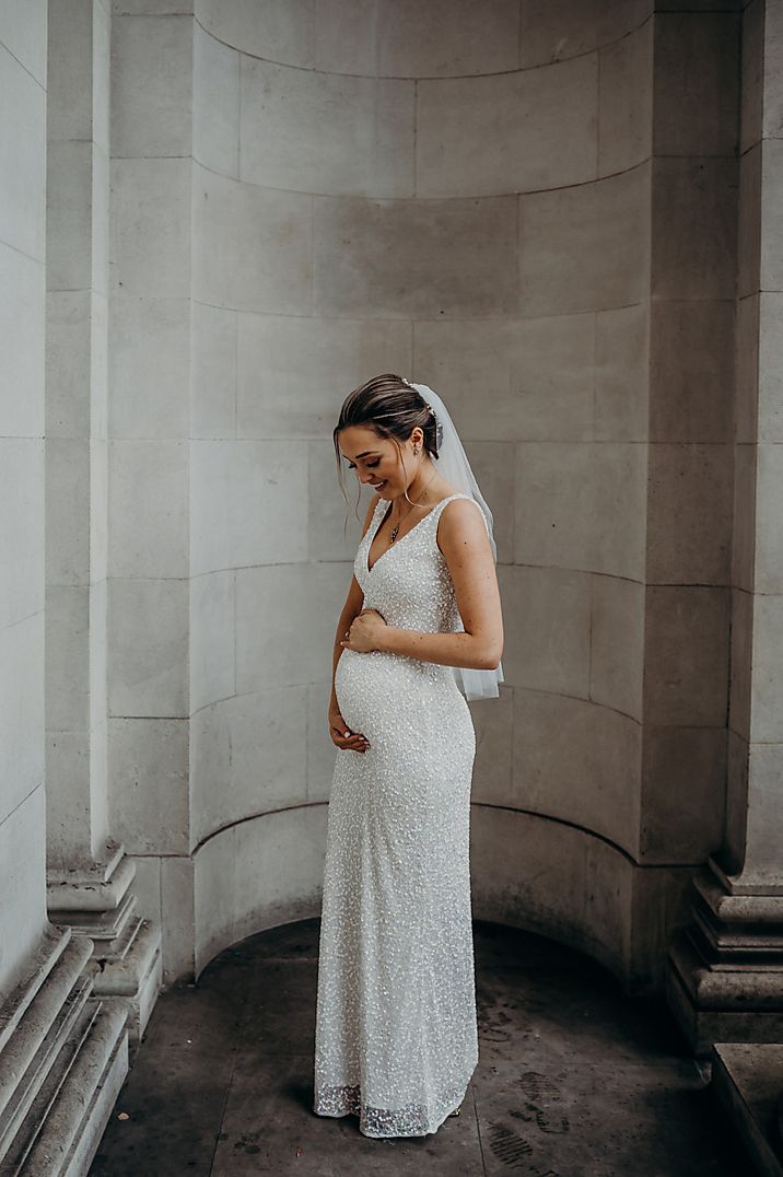 A bride hugs her bump in a sparkling wedding dress 