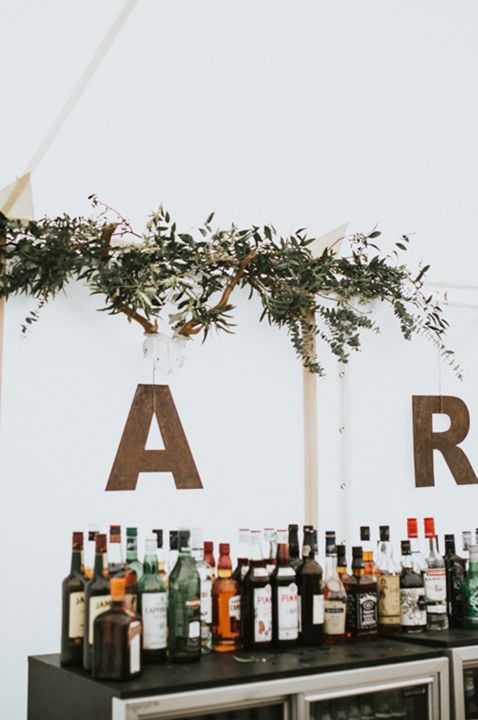 Marquee wedding reception with mini fridges and alcohol bottles with rustic wooden letter lights sign 