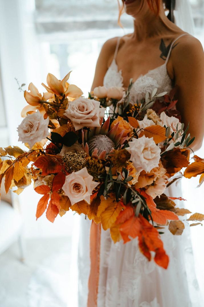 Bride carrying oversized wedding bouquet with orange leaves 