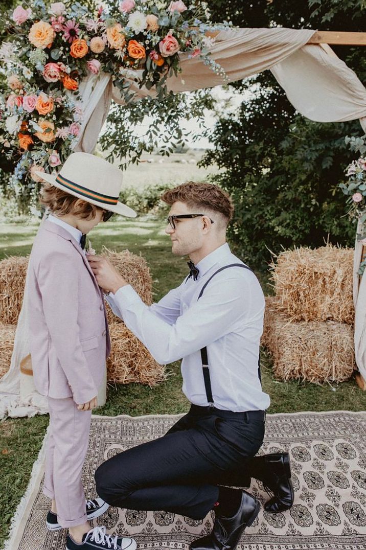 The groom helps the page boy with his bow tie that matches his pink suit at outdoor wedding 