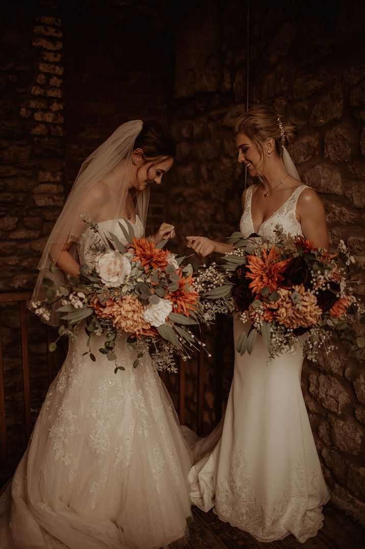 First look with two brides in fishtail wedding dresses holding oversized orange wedding bouquets 