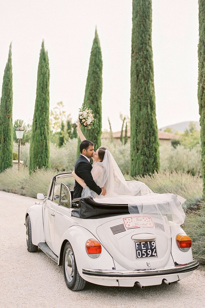 Bride in long veil with groom in convertible VW Beetle wedding car