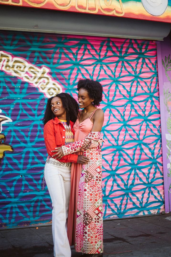 Couple stand in front of a bright and colourful painted garage door 