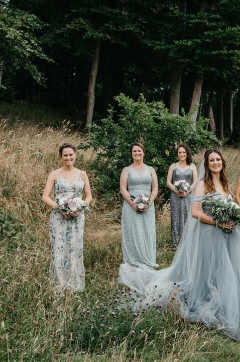 Bride in ethereal tulle blue wedding dress standing in a field with bridal party wearing mismatched blue bridesmaid dresses 