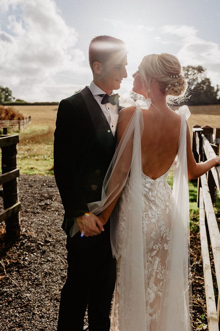 Groom in black tuxedo with bride in low back wedding dress with tulle bow straps with pearl earrings 