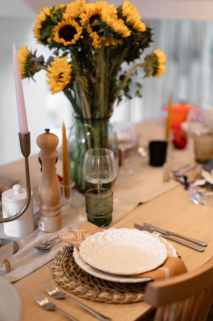 Wicker place mat with patterned white plates with glass vase of sunflowers 