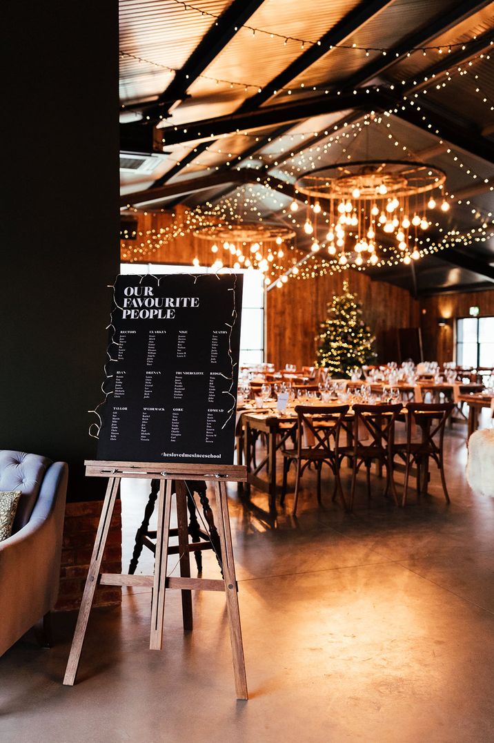 Black and white wedding table plan at the entrance to the cosy wedding breakfast with Christmas tree 