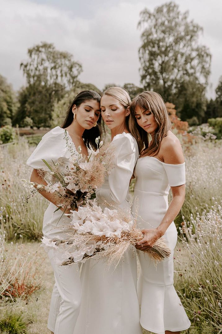 Bridal party wearing midi white bridesmaid dresses and neutral toned bouquets