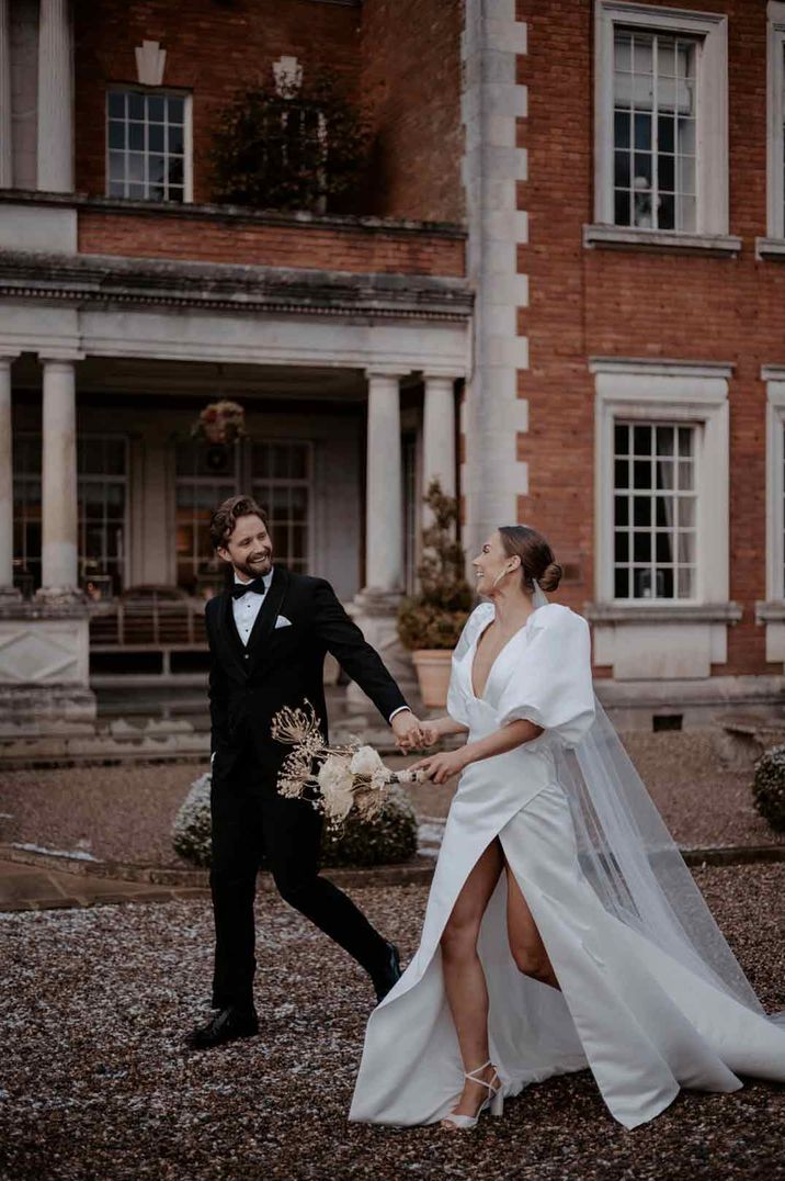 Bride in puff sleeve leg slit wedding dress with church length veil walking with groom in classic black tuxedo - wedding budget spreadsheet 