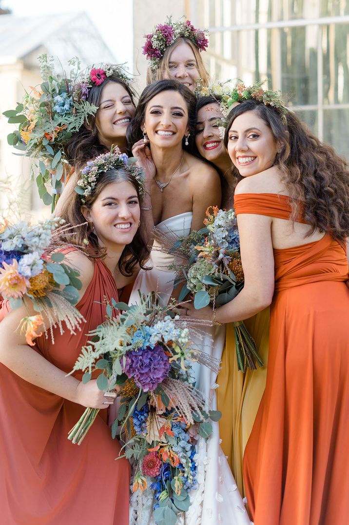 Mismatched bridesmaid dresses in shades of orange for colourful wedding theme with flower crowns 