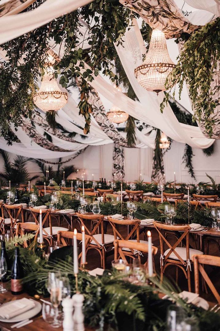 Botanical luxe wedding reception room at Iscoyd Park - suspended foliage, wedding steamers, festoon chandelier lighting, foliage table runners, and tapered candles 