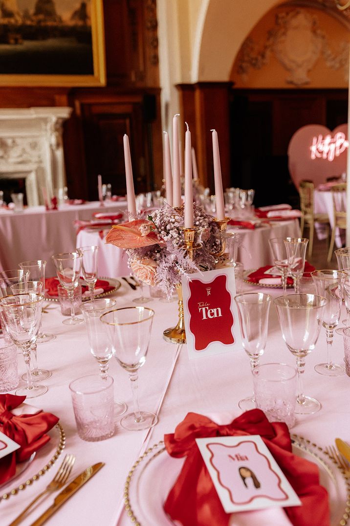 Light pink wedding table cloth and candles with pink and red wedding table number sign and place setting with bows 