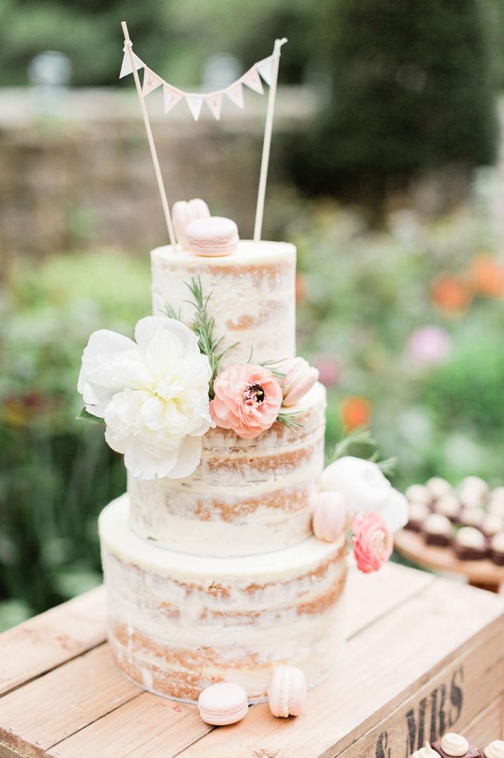 semi naked wedding cake decorated with peach flowers and a burlap bunting cake topper 