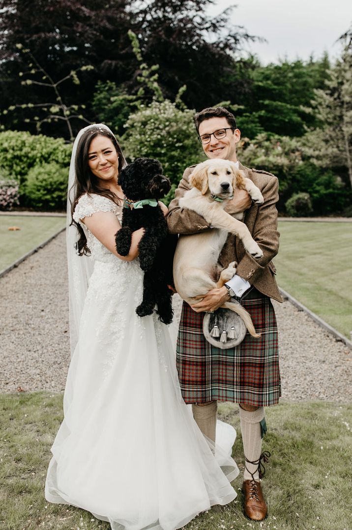 Bride in a tulle and lace princess wedding dress and groom in a kilt holding their pets at their intimate wedding 