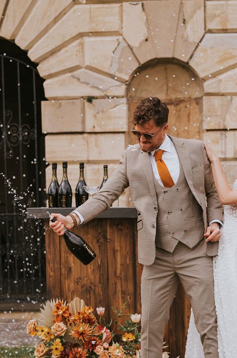 Couple in white headband and lace sleeveless dress and tartan suit popping champagne