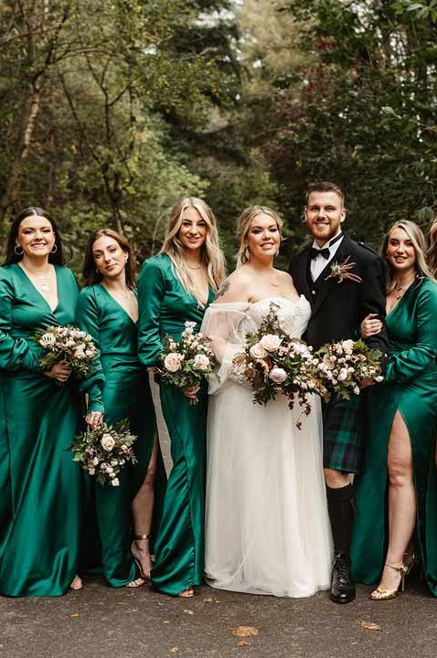 Mixed gender wedding party with bridesmaids in emerald green v-neck long sleeve front slit dresses and male bridesmaid in dark suit and black bowtie