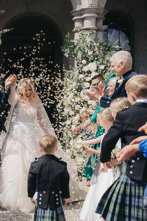 Bride in mesh long sleeve wedding dress doing confetti exit with groom in wedding kilt and sporran at Cluny Castle wedding venue Scotland 