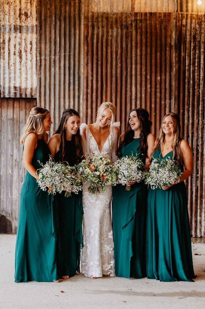 Bride in low v-neck lace wedding dress standing with bridesmaids in bottle green mismatched bridesmaid dresses