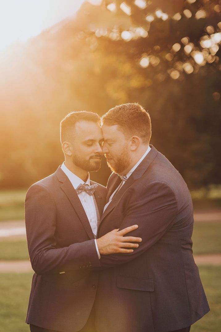 Two grooms embrace each other as gorgeous natural golden light shines behind them