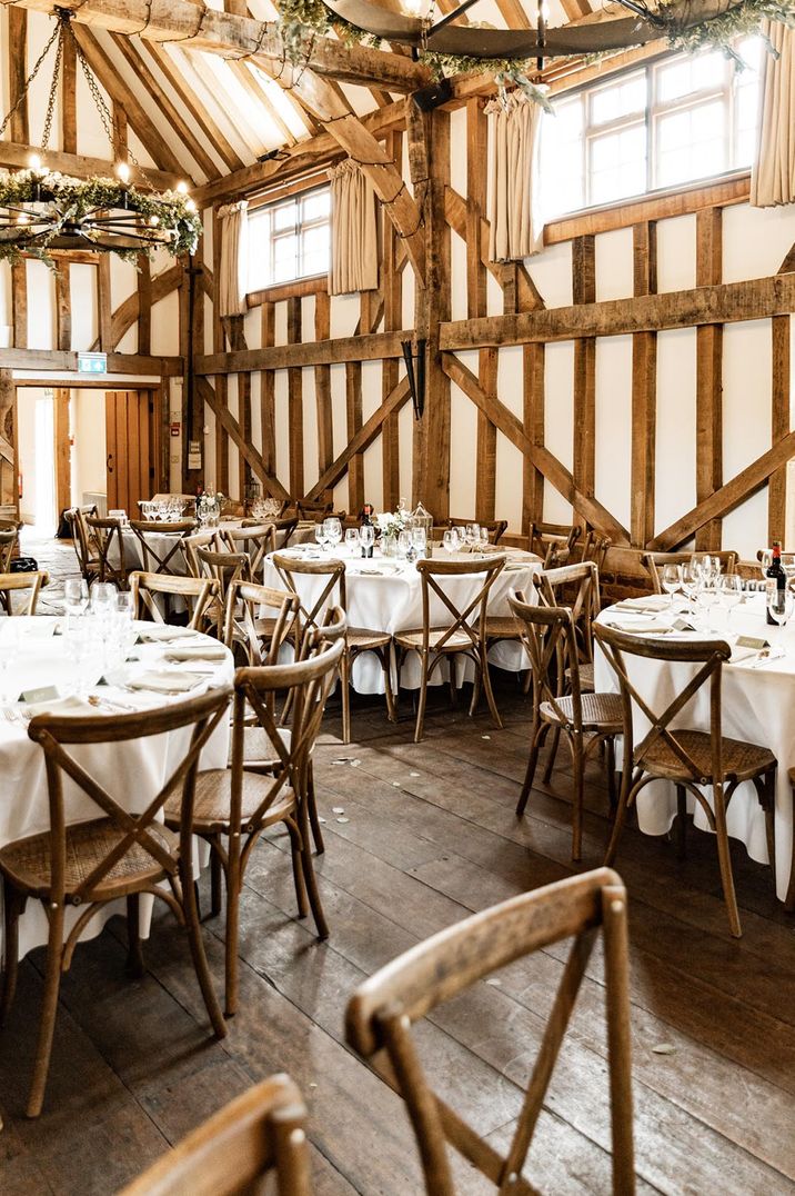 Rustic barn wedding venue with round tables decorated with white tablecloths and chandeliers 