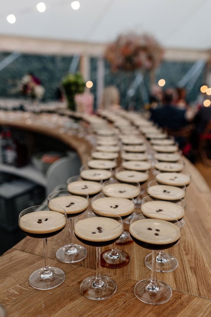 Wooden bar lined with rows of espresso martini cocktail drinks 