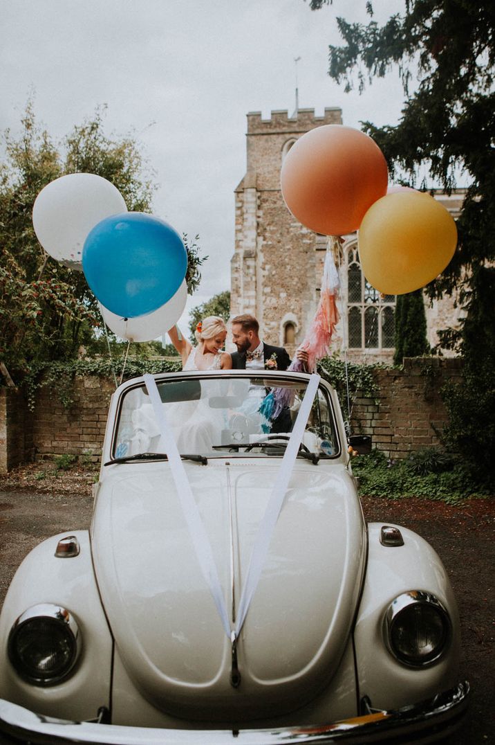 Bride and groom in a convertible Beetle holding giant colourful balloons 