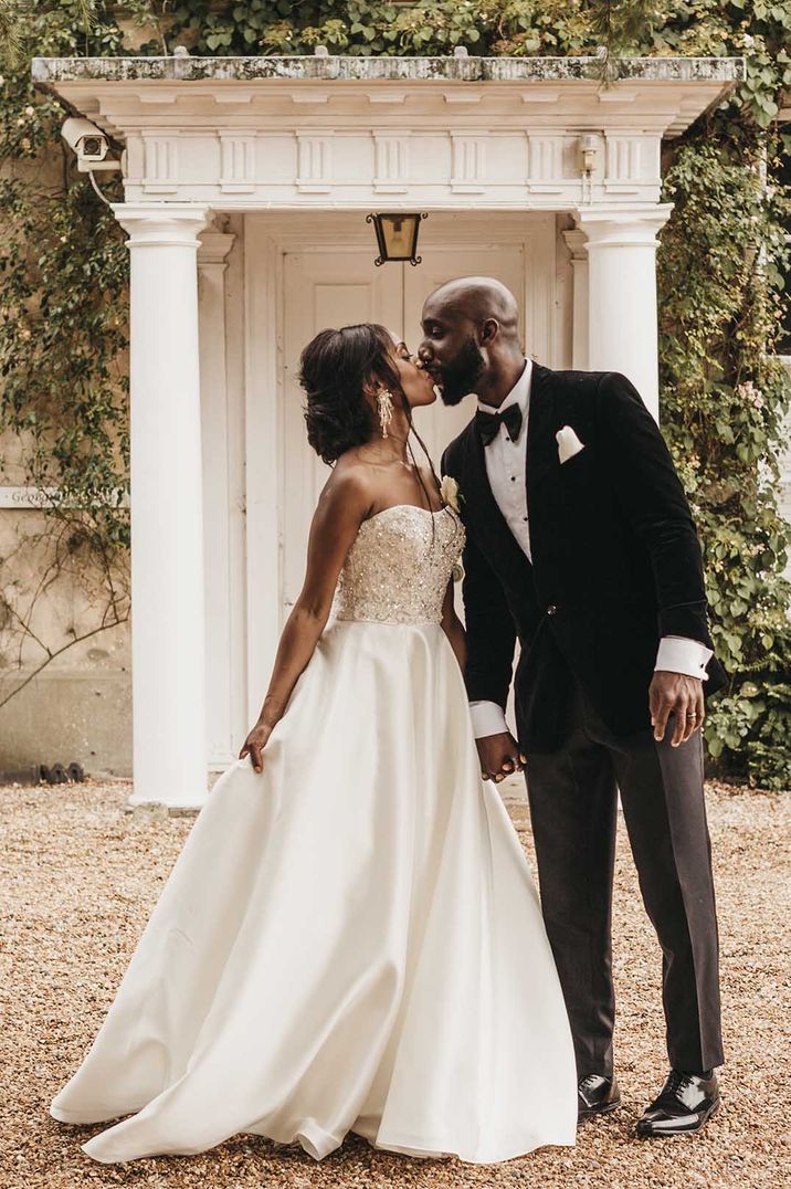 Bride in strapless wedding dress and cathedral length veil kissing her groom