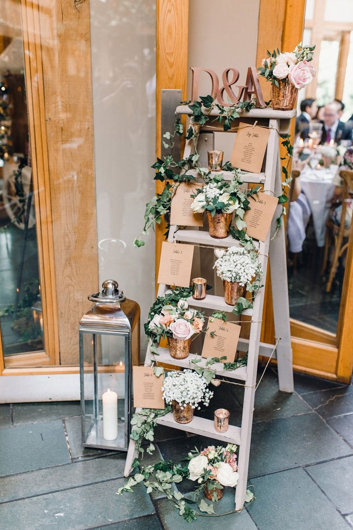 Grey wooden stepladder seating chart with flowers, foliage and candles 