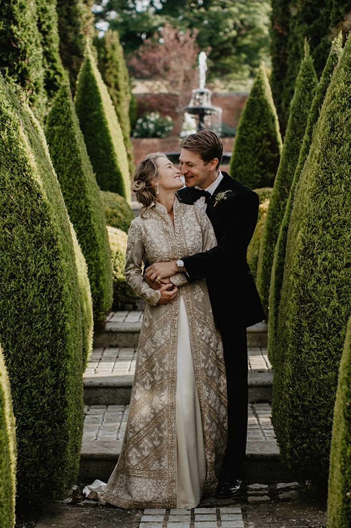 At home wedding with the bride wearing a traditional Indian bridal coat kissing the groom for couple portraits 