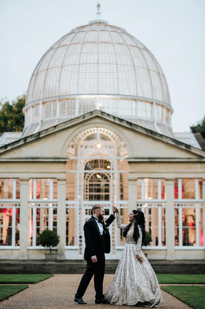 Bride in long sleeve sparkly wedding dress and groom in classic tux dancing outside of Syon Park glasshouse wedding venue 