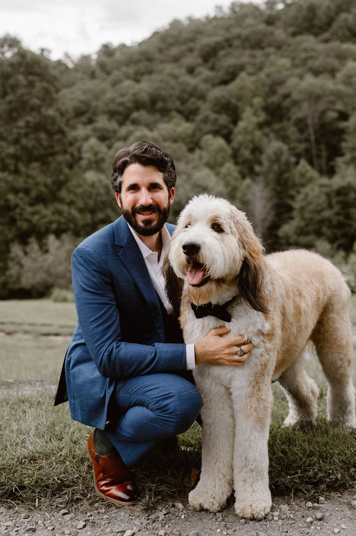 Groom in dark blue wedding suit petting his dog at the dog friendly wedding venue 