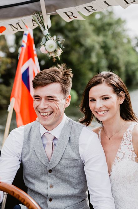 Groom in a grey waistcoat and bride in a lace wedding dress riding a boat along the river