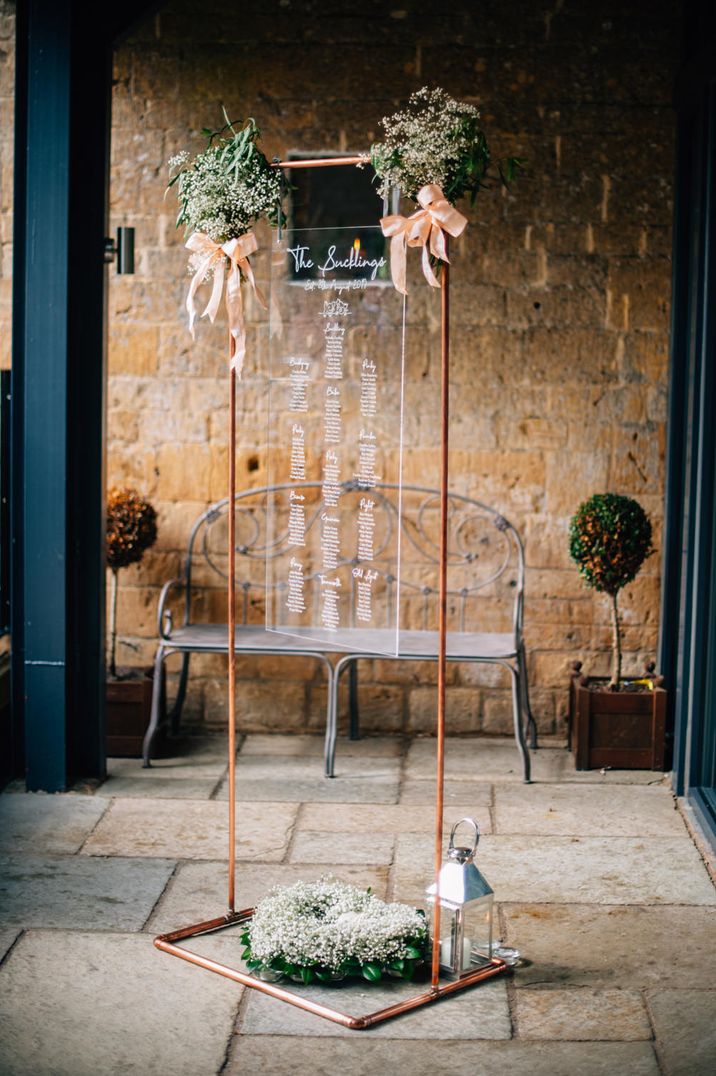 Copper frame and perspex wedding table plan with peach ribbon decor 