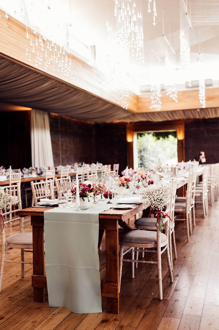 Traditional wedding reception room with sage green table runners, pink and red florals and white bamboo chairs at Elmore Court 