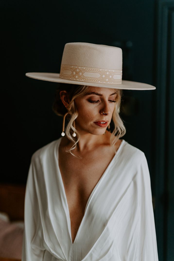 Bride wearing cream hat with wishbone earrings and drape wedding dress