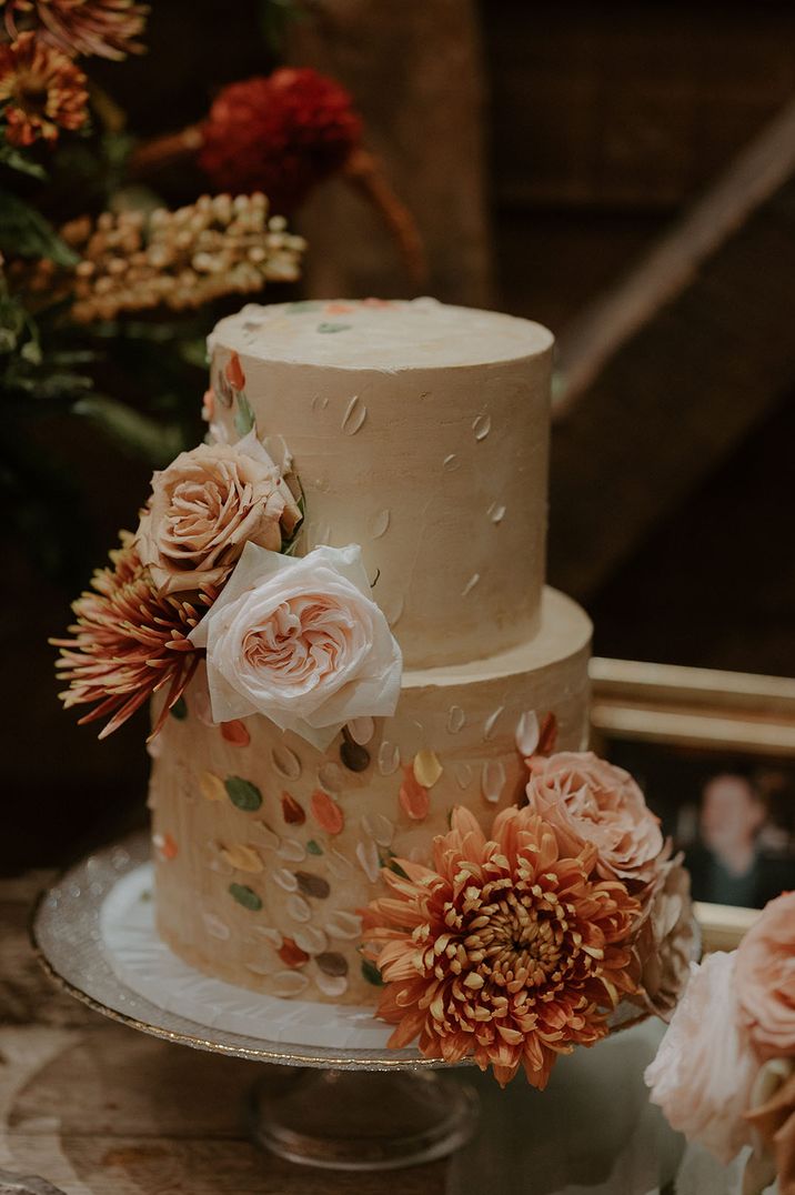 Two tier simple white frosted wedding cake with colourful iced petals by Terre Et Lune Cake Design