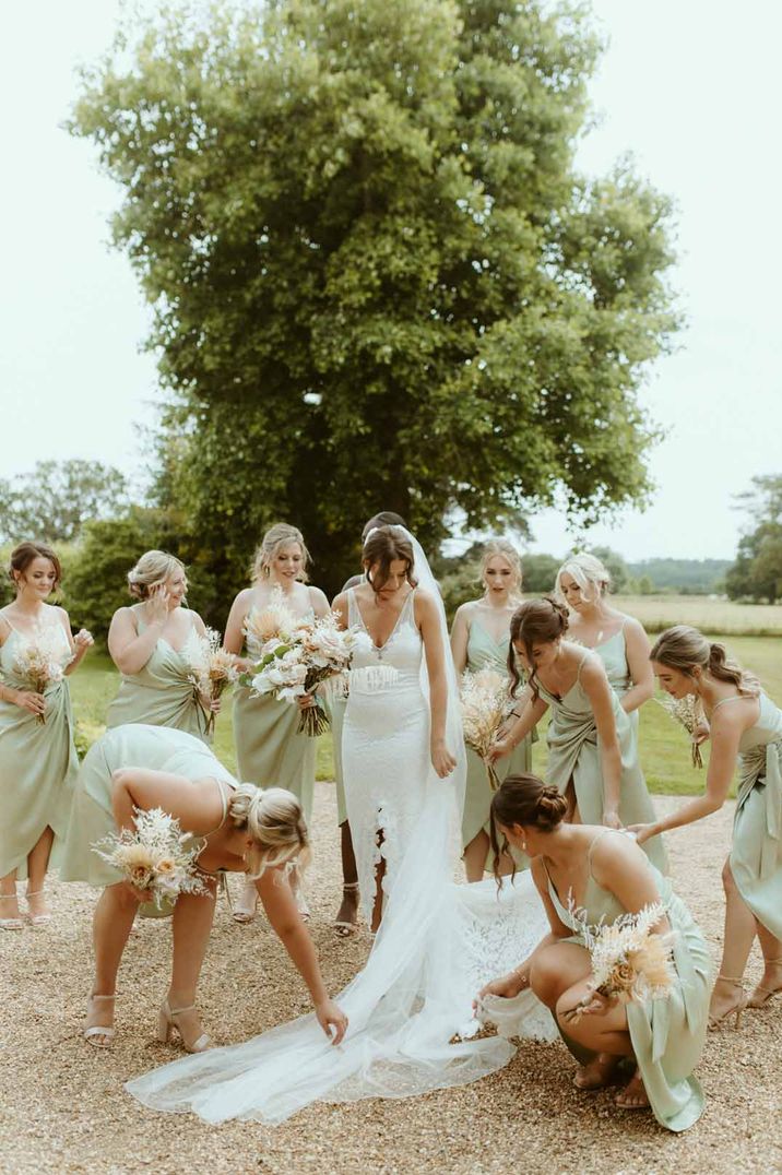 Bridesmaids in light green satin front twist bridesmaid dresses helping bride in v neck lace wedding dress with front slit and church length veil 