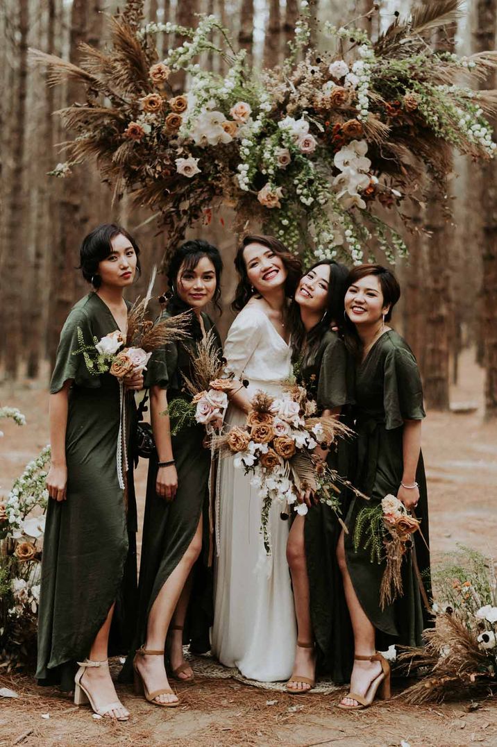 Bridesmaids standing with bride wearing forest green short sleeve front slit bridesmaid dresses in the forest 