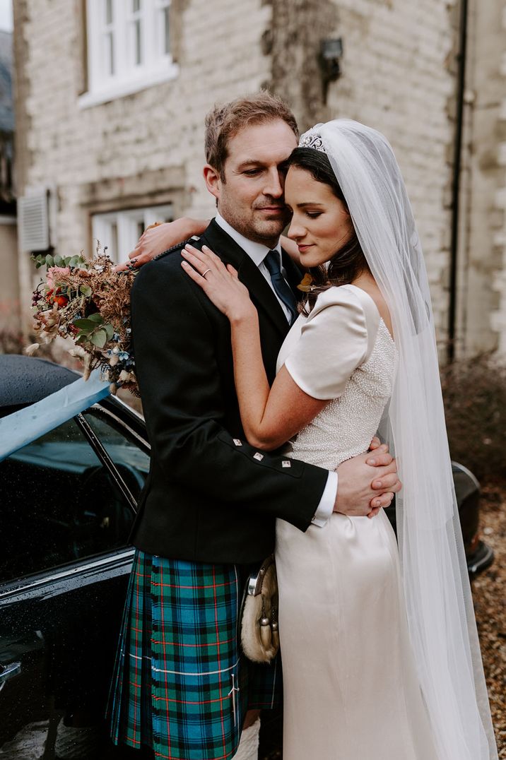 Bride wearing satin short sleeve wedding dress with pearl top embracing groom at Christmas festive wedding 