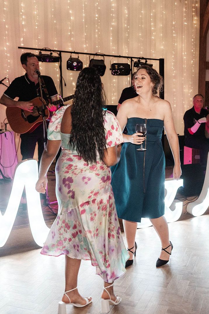 Wedding guests wearing floral and teal dresses dancing at the wedding reception 