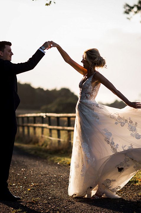 Bride in floral lace wedding dress with the groom in a black tuxedo dancing together 